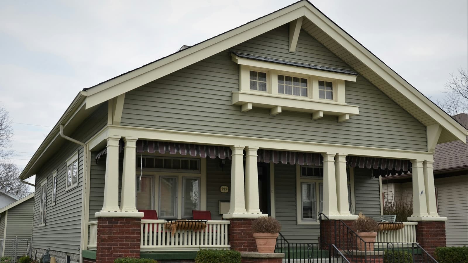 Craftsman bungalow with green siding and brick porch columns